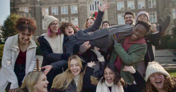 A group of students smile and laugh while holding up another student sideways.