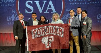 Seven people stand together and hold a maroon flag that says "Fordham."