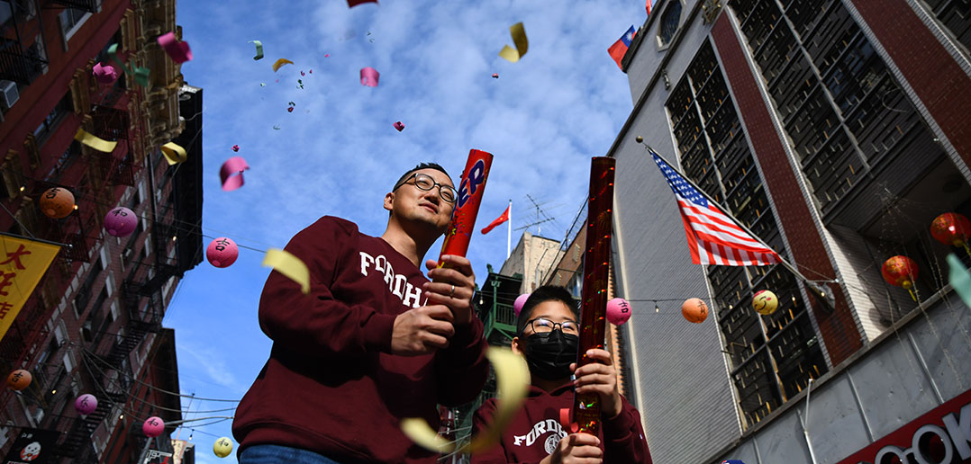 Wearing maroon Fordham sweatshirts, Mark Son, a 2010 Fordham Law graduate, and his son Aaron set off confetti poppers against a blue sky during Lunar New Year celebrations in Manhattan on February 12, 2022.