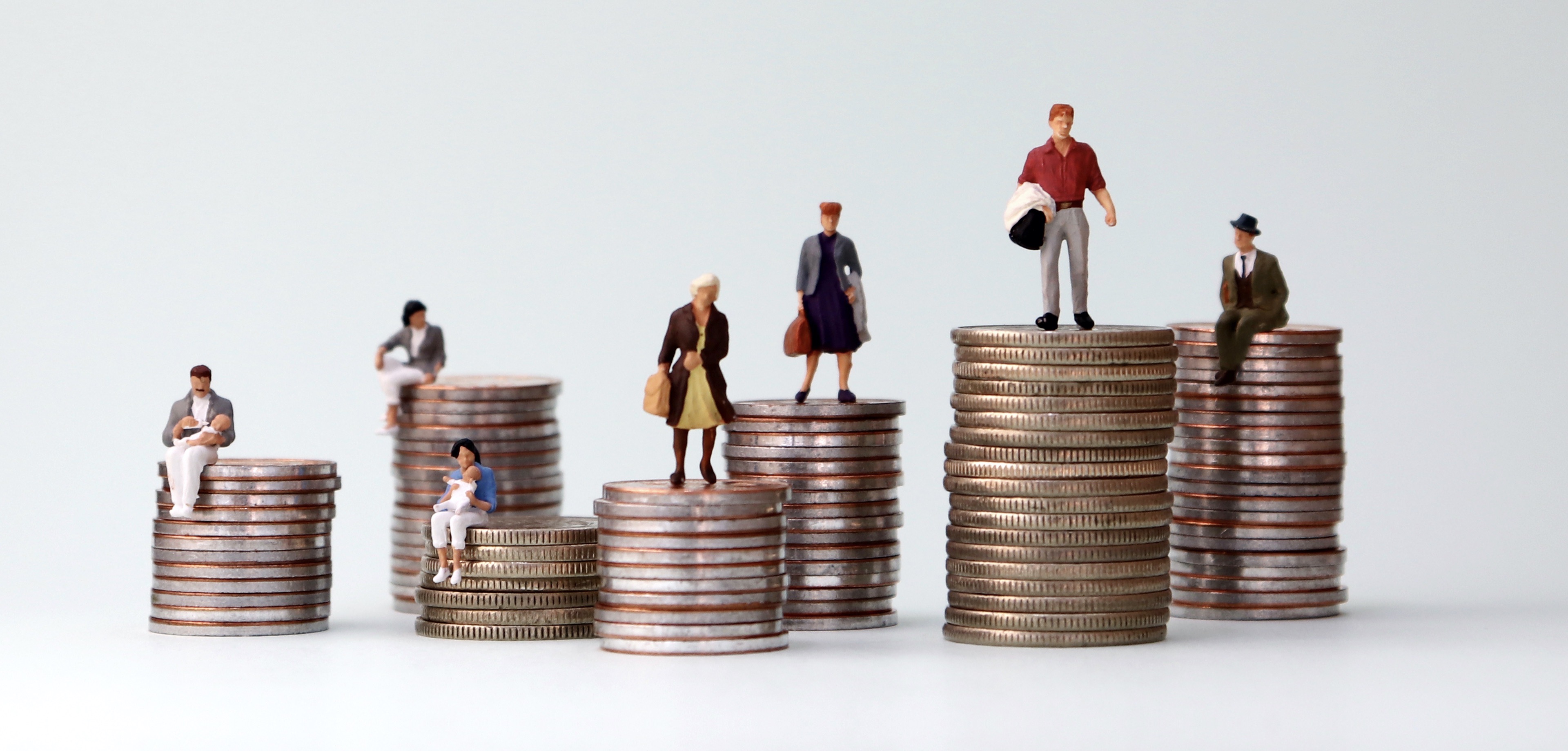 Miniature people standing on piles of different heights of coins. Income and economic inequality concept.