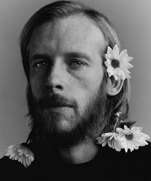 A press photo of Kevin Devine with flowers in his hair.