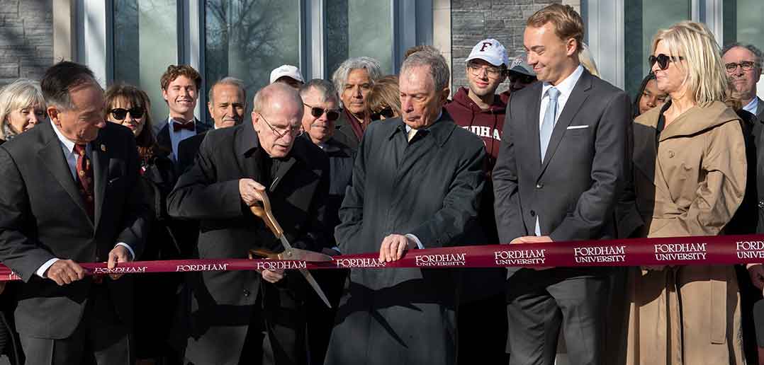 Father McShane cuts a ceremonial ribbon as Michael Bloomberg and others look on.