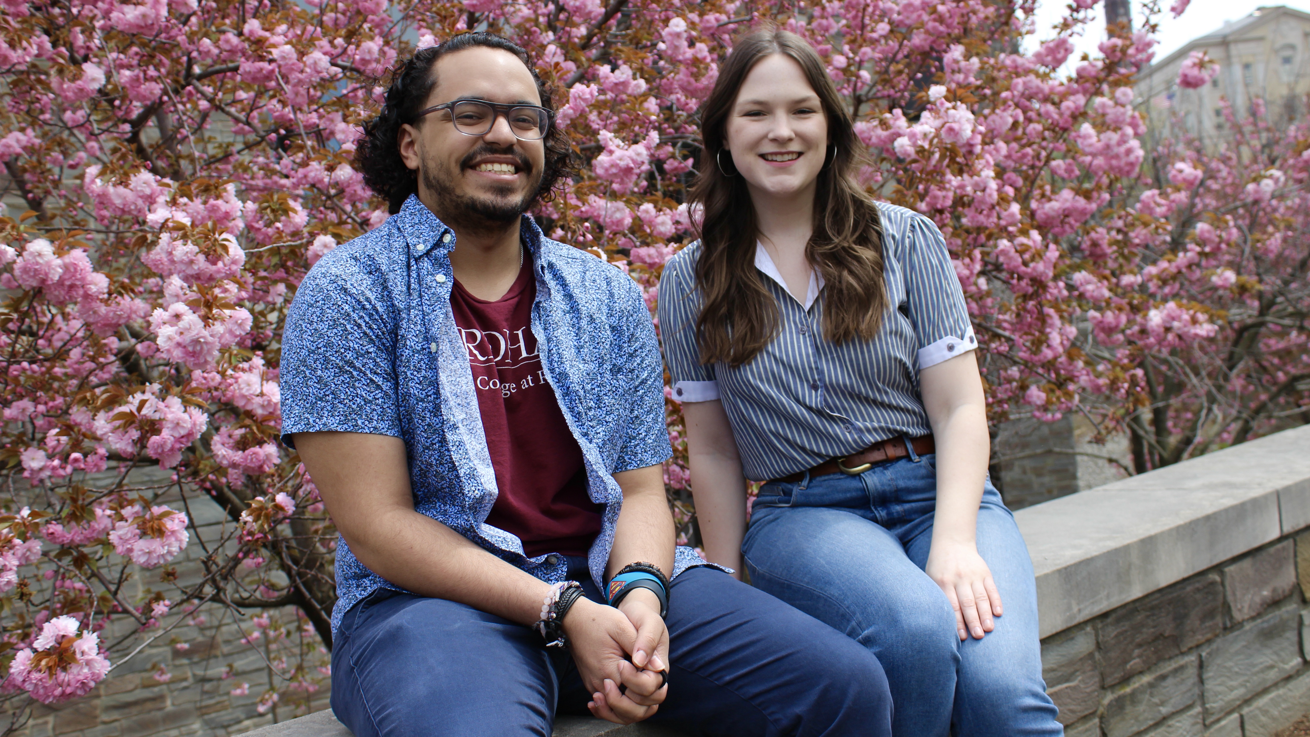 A man and woman smile in front of pink cherry blossom trees.