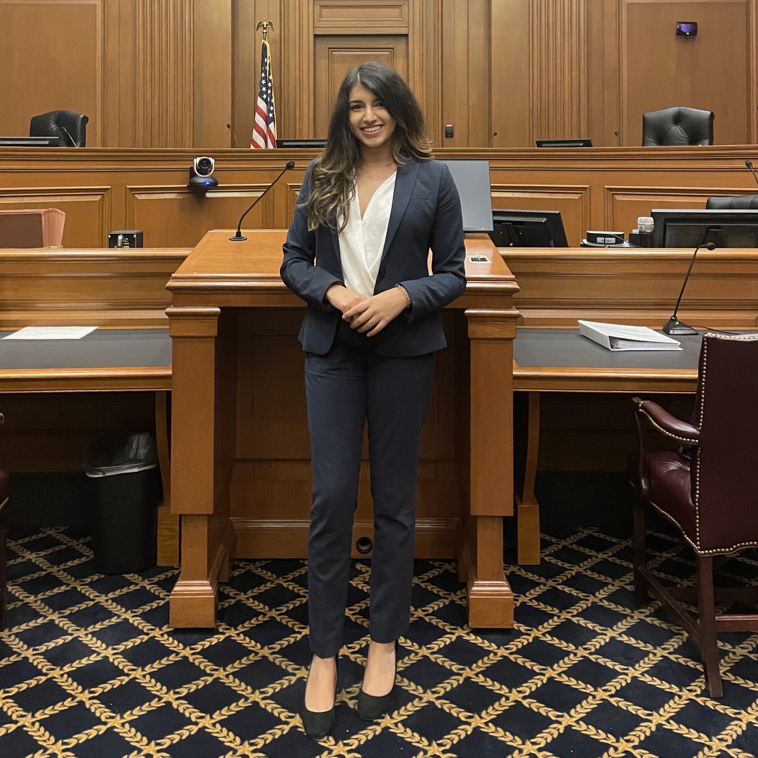 A woman wearing a black business suit smiles and stands in a courtroom.