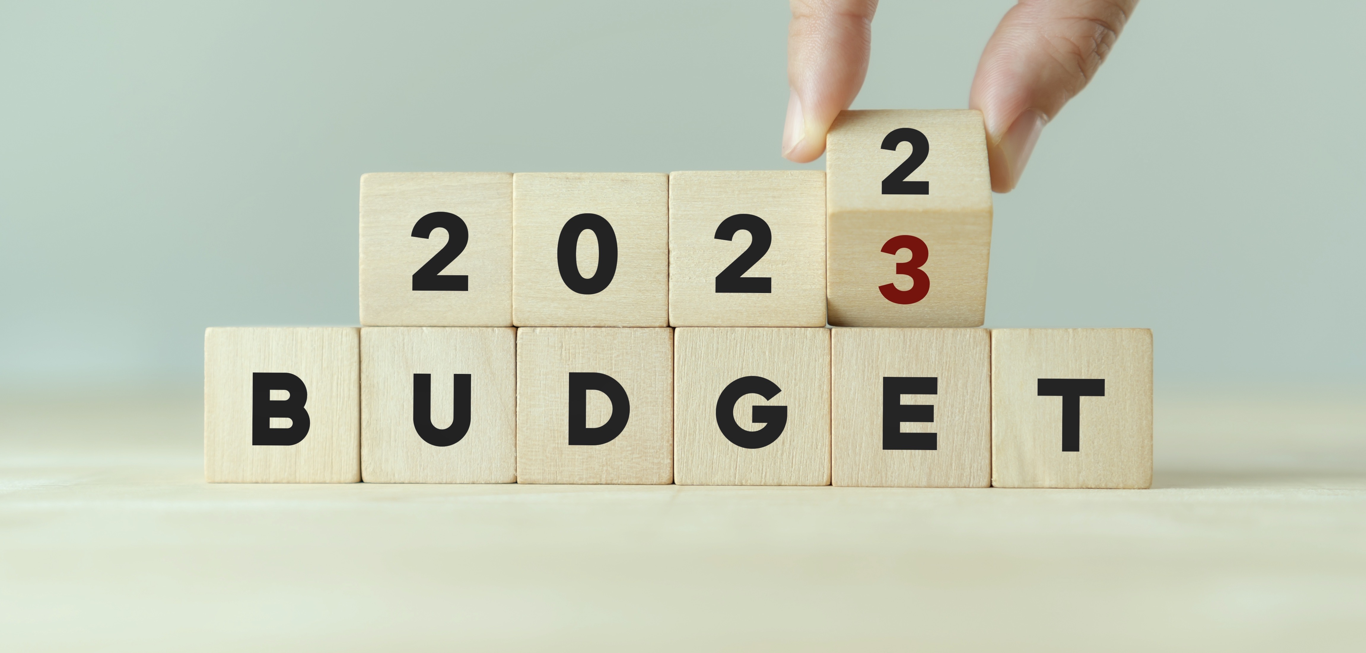 2023 Budget planning and allocation concept. Hand flips wooden cube and changes the inscription "BUDGET 2022" to "BUDGET 2023" with grey background, copy space.