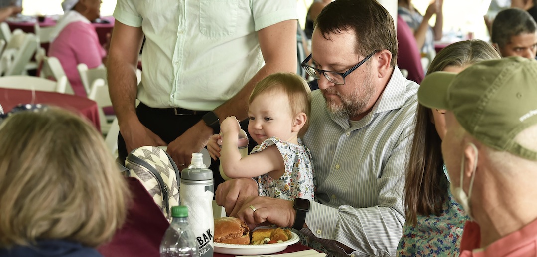 A man holds a baby and eats food.