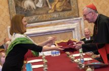 A woman gives a maroon baseball cap to a man wearing a priestly outfit.