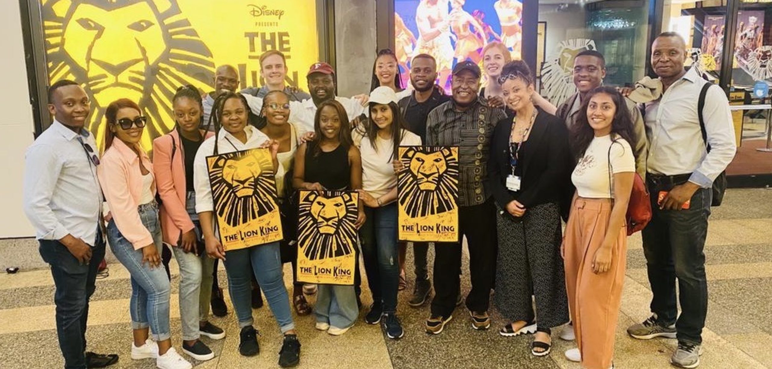 A group of people smile while holding posters of a yellow cartoon lion.