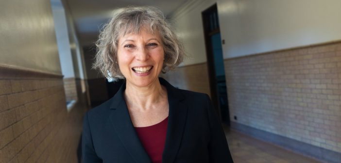 A woman with gray hair smiles in a school hallway.