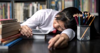 Student teen sleeping sit at table at library study online on laptop with textbook