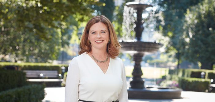 A portrait of Fordham President Tania Tetlow outside Cunniffe House with Cunniffe Fountain in the background
