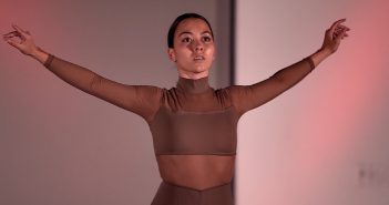 A woman wearing a bodysuit spreads her arms out dramatically.