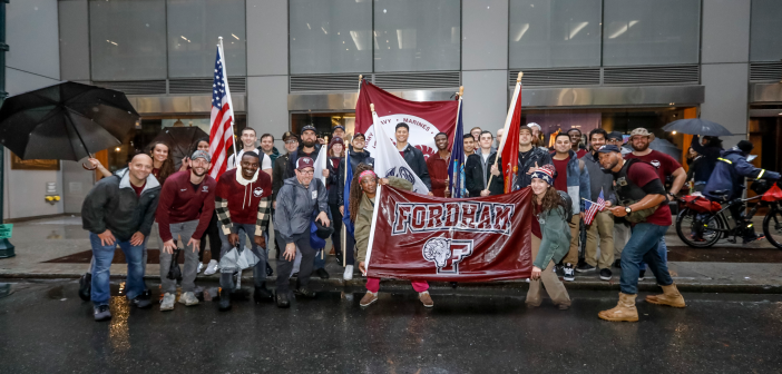 Group photo of Fordham veterans and guests outside, holding Fordham sign and the American flag, along with Fordham flags