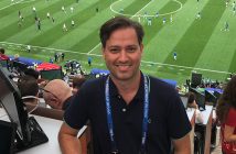 Journalist and Fordham graduate Clemente Lisi in the press area at a match during the 2018 World Cup in Russia, with a match being played on the field behind him