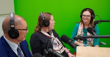 Three seated people wearing headphones speak into microphones.
