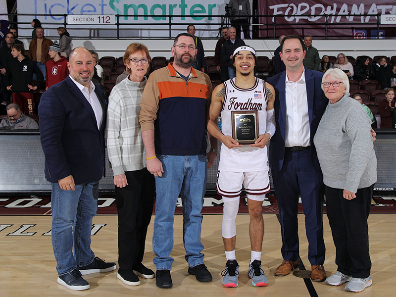 Following the Rams' victory against Stonehill College in the Tom Konchalski Classic, Fordham guard Darius Quisenberry (third from right) received the tournament's Jim O'Connell Most Outstanding Player award. He was joined on the court by (from left) Fordham athletic director Ed Kull and members of the O'Connell family: Jim's wife and Fordham Athletics Hall of Fame, Anne Gregory O'Connell, FCRH '80; their sons, James and Andrew, FCRH '12; and his sister Mary. Photo courtesy of Fordham athletics