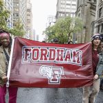 Two women holding the Fordham sign as they march in the parade. One women is on each side.