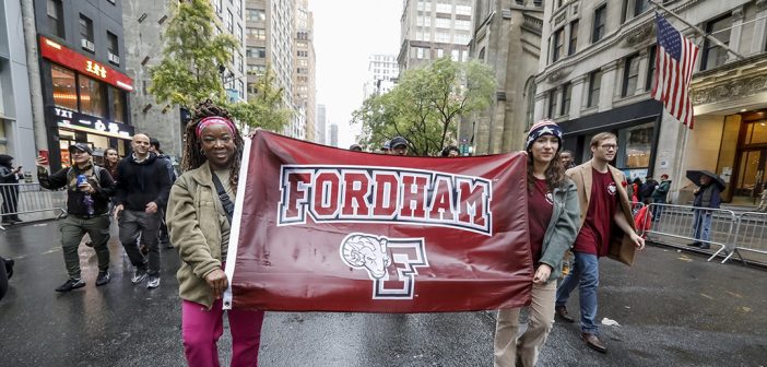Two women holding the Fordham sign as they march in the parade. One women is on each side.