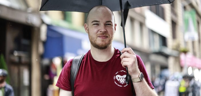 Man wearing a maroon Fordham vets shirt, holding an umbrella smiling.