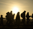 many people waling in a line with the sun setting