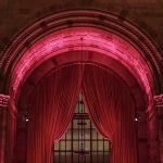 A pink curtain surrounded by two bright Christmas bell lights.