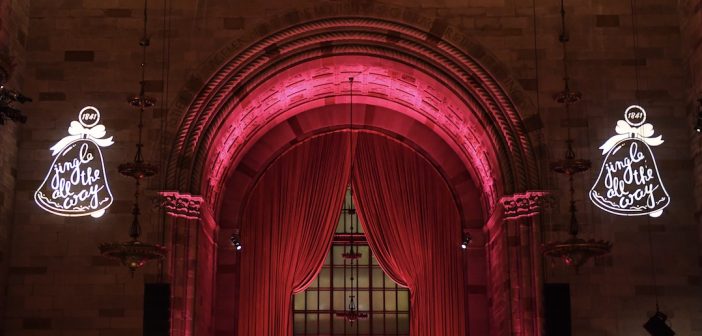 A pink curtain surrounded by two bright Christmas bell lights.