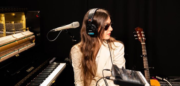 The artist Weyes Blood in white blazer and sunglasses at a piano during a live performance in Studio A at WFUV, Fordham University's public media station, in May 2019