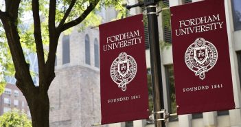Two maroon flags saying "Fordham" hang in front of trees.