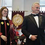 A woman in graduation robes and a man in a suit smile