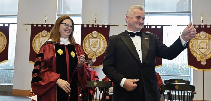 A woman in graduation robes and a man in a suit smile