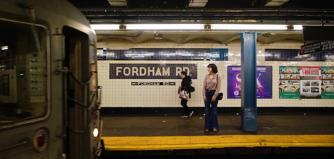 A girl stands on a subway platform and looks in the direction of an oncoming train.