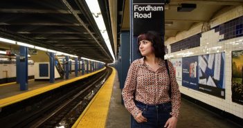 A girl stands on a subway platform and leans against a pillar.