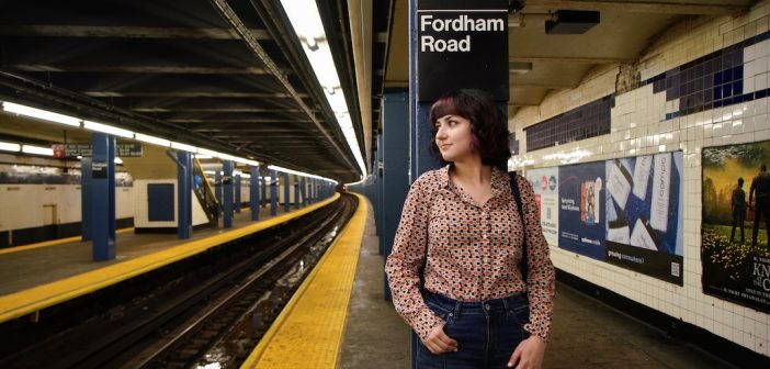 A girl stands on a subway platform and leans against a pillar.