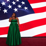 Young woman in green gown singing on front of American flag