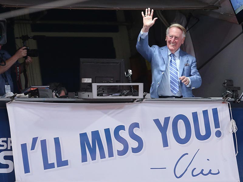 Vin Scully waves to fans from the broadcast booth at Dodger Stadium on September 24, 2016, during his final homestand as the Dodgers' broadcaster. Underneath him hangs a sign that reads, "I'll miss you."