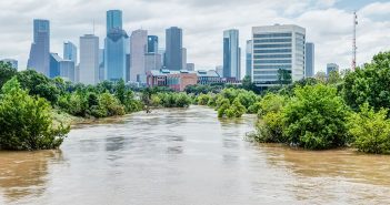 High and fast water rising in Bayou River with downtown Houston in background under cloud blue sky. Heavy rains from Harvey Tropical Hurricane storm caused many flooded areas in greater Houston area.