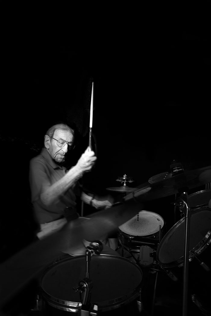 A black-and-white portrait of Holocaust survivor Saul Dreier playing the drums