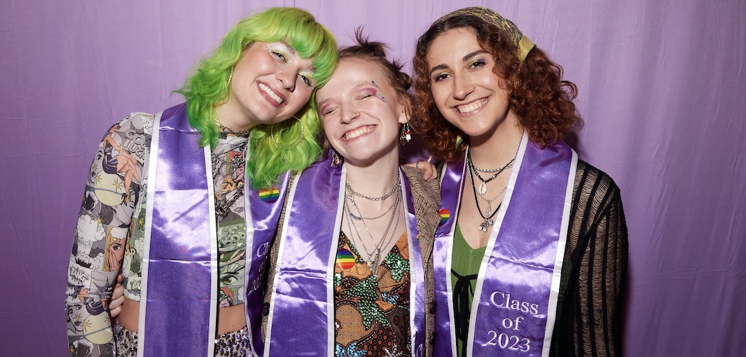 Three women wearing lavender stoles smile in front of a lavender backdrop.