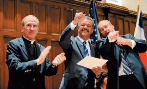 Father McShane (left), President of the Dominican Republic (center) and another man to the right. They are all smiling and in professional attire. 