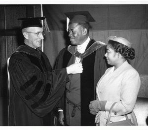 Two men in cap and gown, a woman in regular clothes to their left.