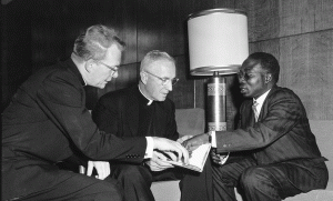 3 men sitting on couch pointing at a book.