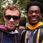 Two Fordham graduates in cap and gown smile at the camera on their graduation day
