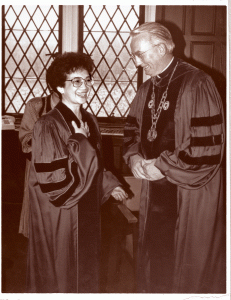 Woman shaking hands with a man. Both in academic robes. 