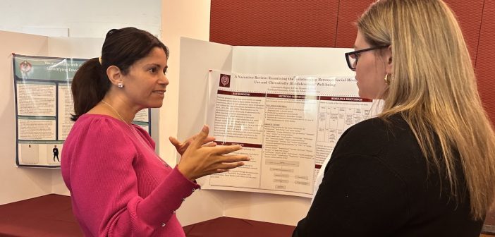 Two people talk in front of a poster board.