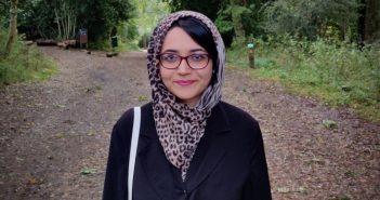 Mishal Ahmed stands in the middle of a forest and smiles.
