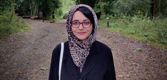 Mishal Ahmed stands in the middle of a forest and smiles.
