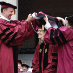Woman being hooded on Commencement stage in maroon robes