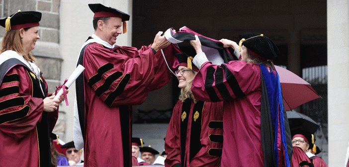 Woman being hooded on Commencement stage in maroon robes