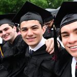 Four man graduates in caps and gowns smiling