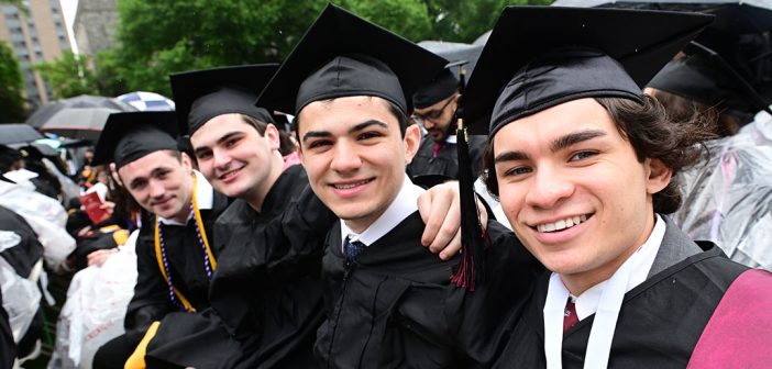 Four man graduates in caps and gowns smiling